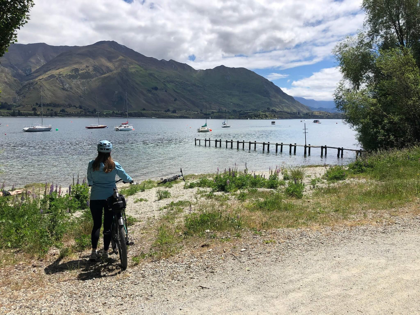 Cyclist pausing beside Lake Hawea on a rugged trail