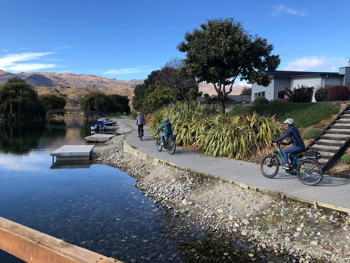 Cyclists riding e-bikes along a lakeside path with mountains and homes