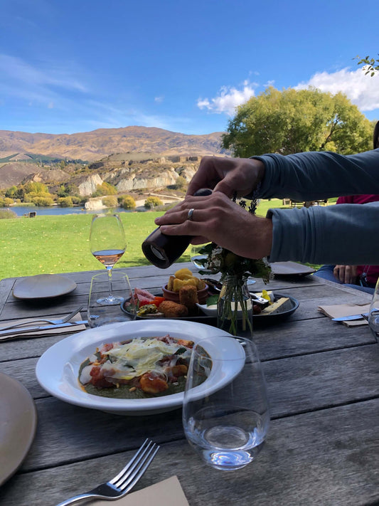 Outdoor dining with gourmet food and wine overlooking Bannockburn cliffs and vineyard views.